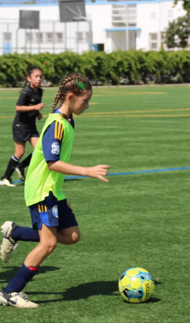 A girl in yellow and blue soccer uniform running on the field.